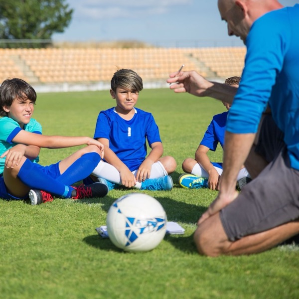 A coach kneeling on the grass walking young players through the plan