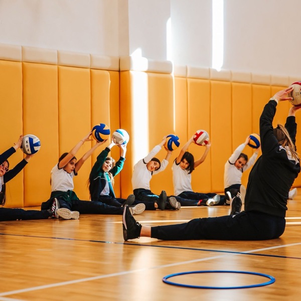 Young volleyball players stretching with their coach in a gym